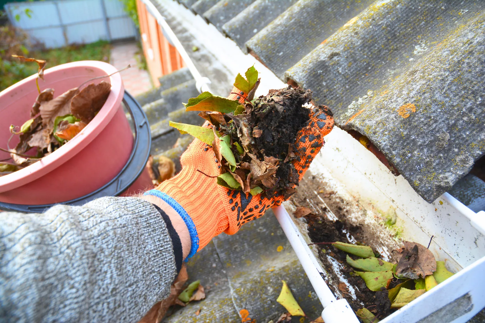 Cleaning debris from a roof gutter, illustrating how granules and buildup can signal roofing problems.